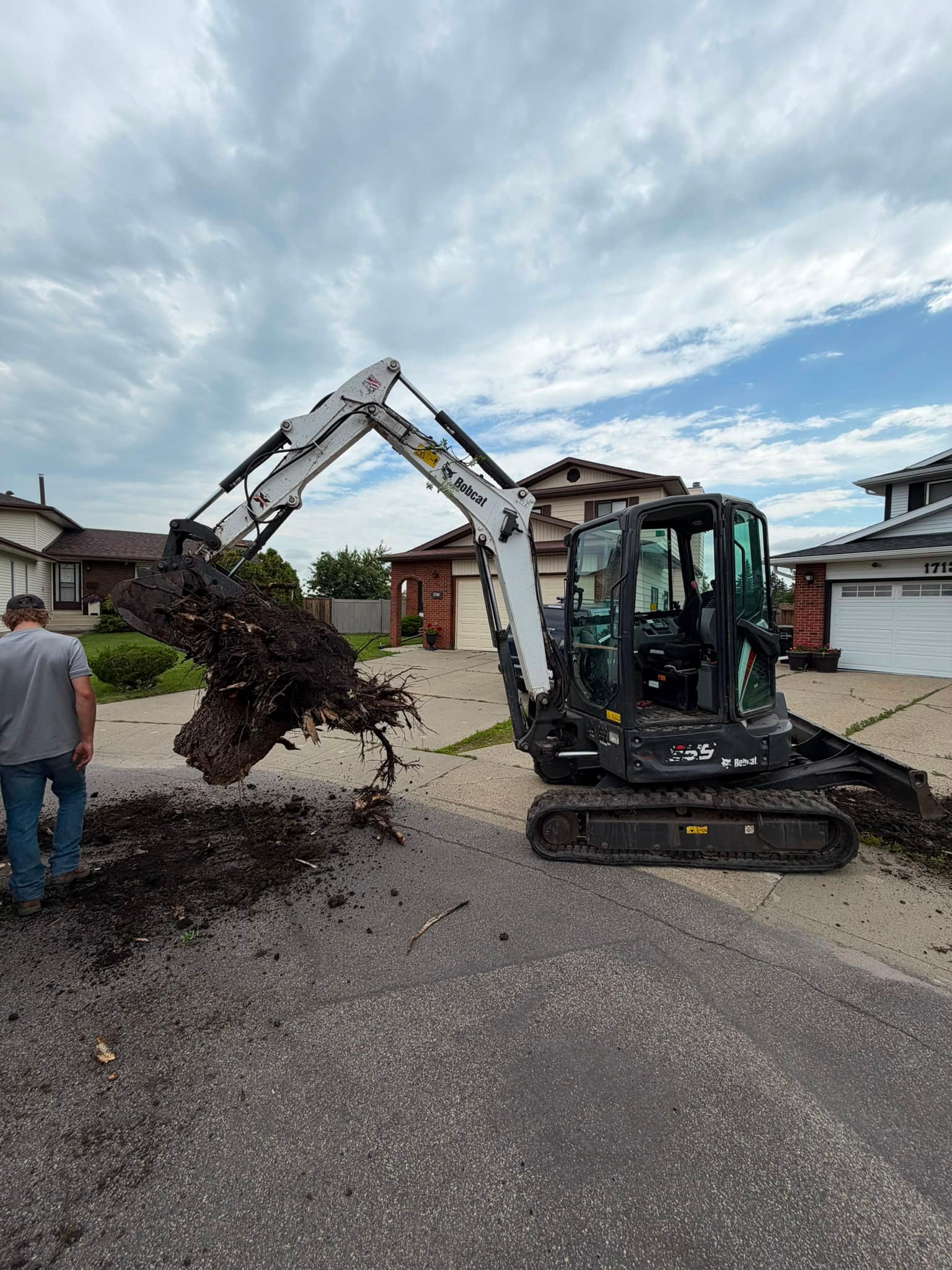 Bobcat E35 mini excavator lifting a tree stump on a residential street